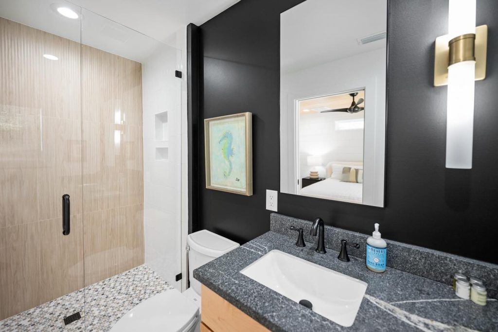 modern bathroom interior shot with granite countertop, black backslash, mirror, and walk in shower